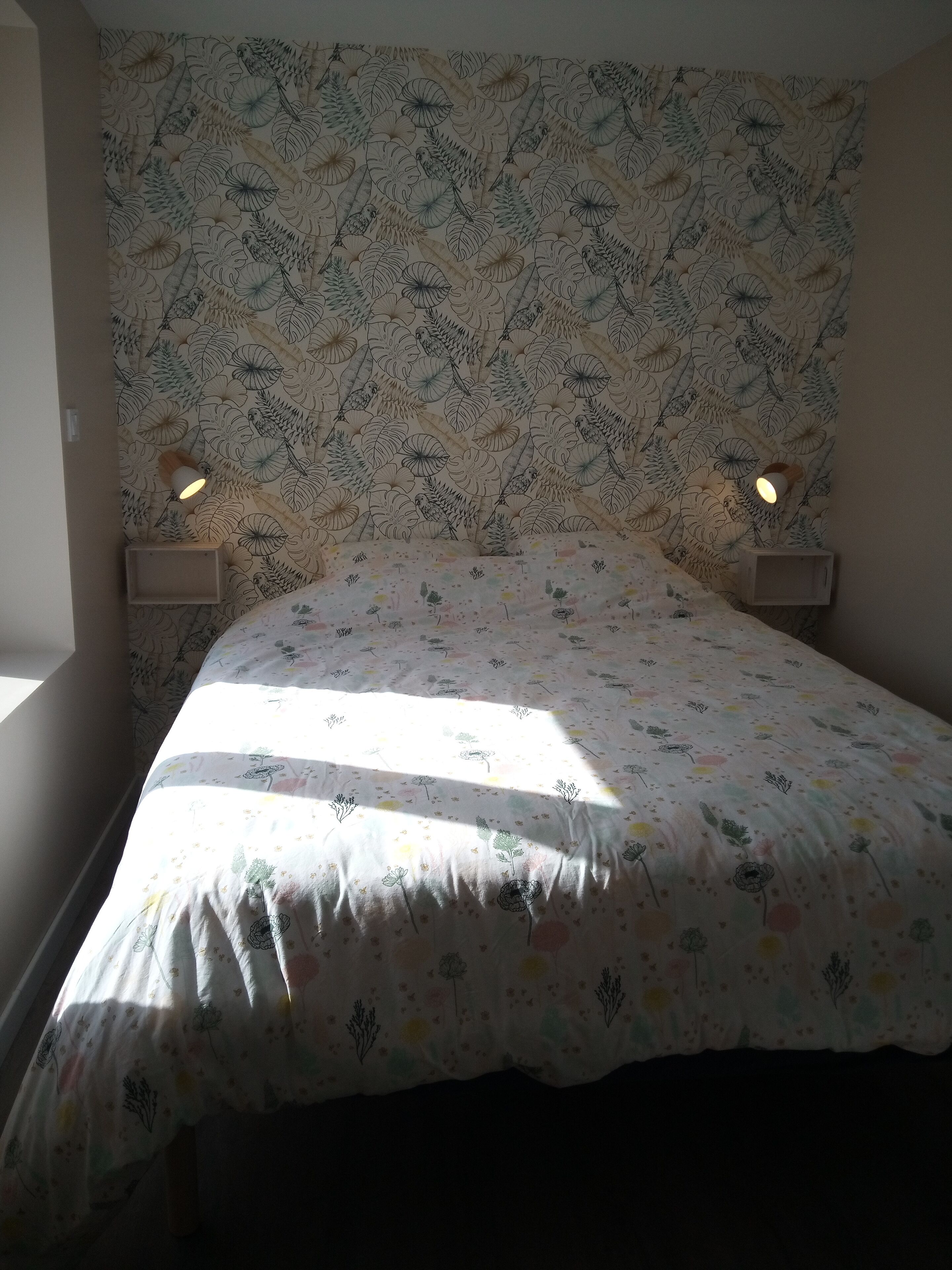 A bedroom with a floral-patterned headboard, a bed with a colorful floral bedspread, and two bedside lamps.