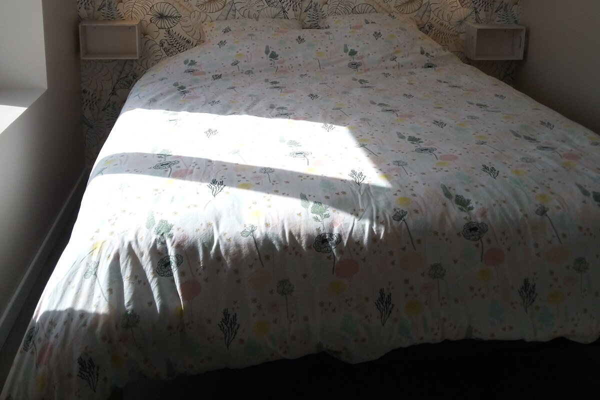 A bedroom with a floral-patterned headboard, a bed with a colorful floral bedspread, and two bedside lamps.