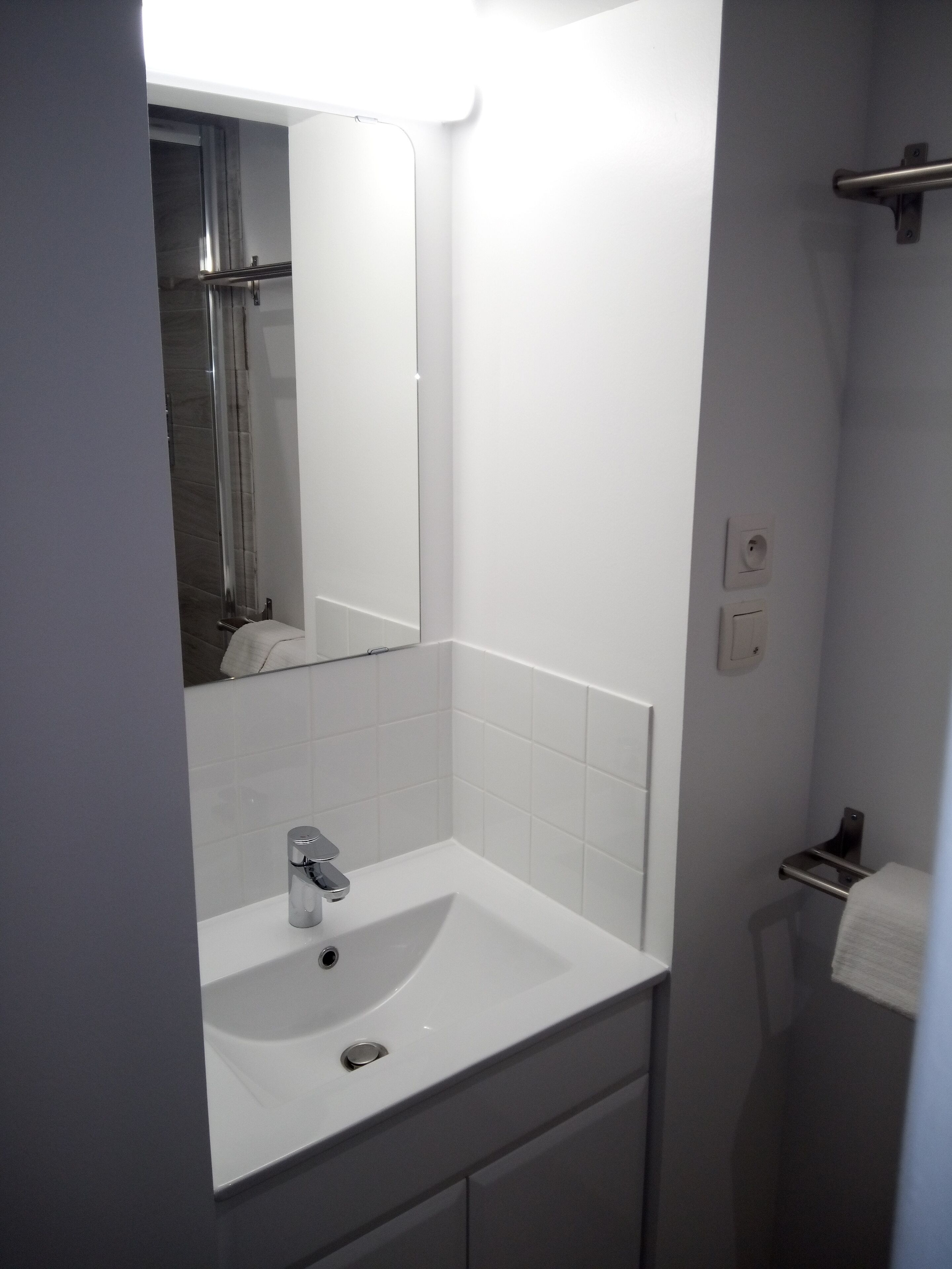 Ein modernes Badezimmer mit Waschbecken, Spiegel und Dusche in Weiß.