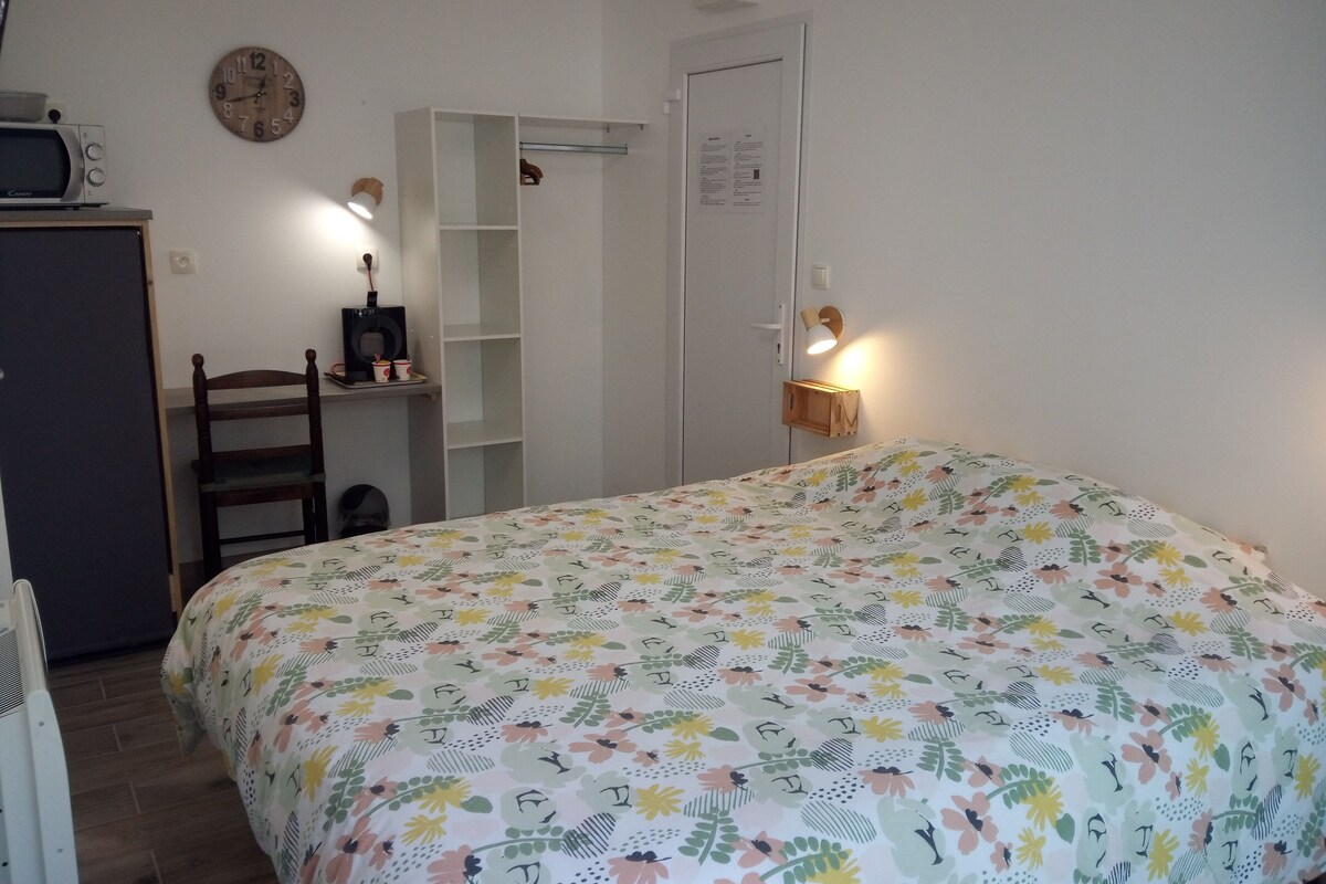 A bedroom with a floral bedspread, a wooden chair, a desk with a microwave, and a wardrobe.