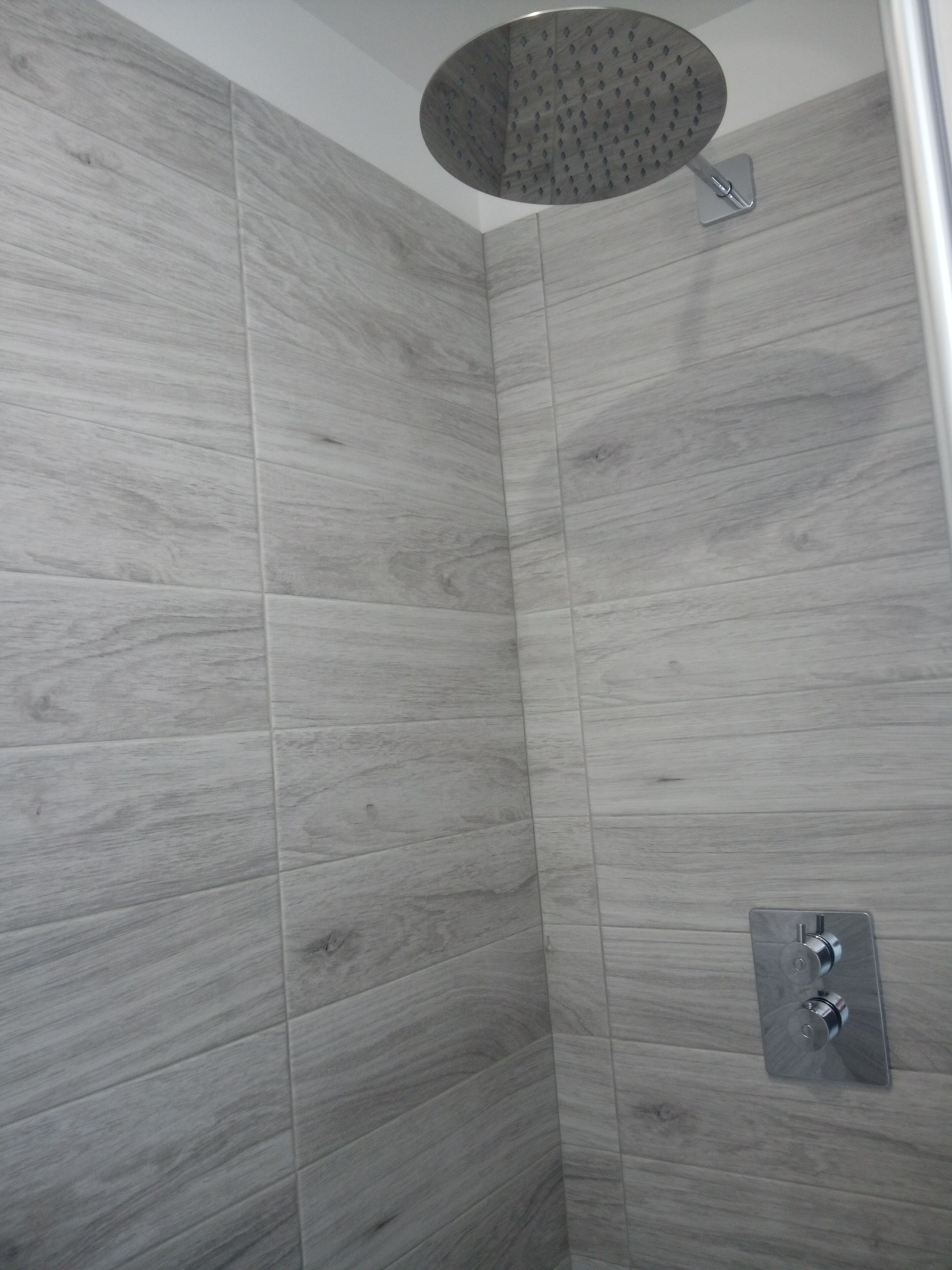 A shower with a round head and a control panel with two knobs.