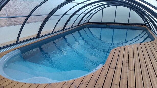 A swimming pool with a wooden deck and a glass ceiling.