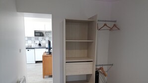 A room with a wooden wardrobe, a radiator, and a kitchen in the background.