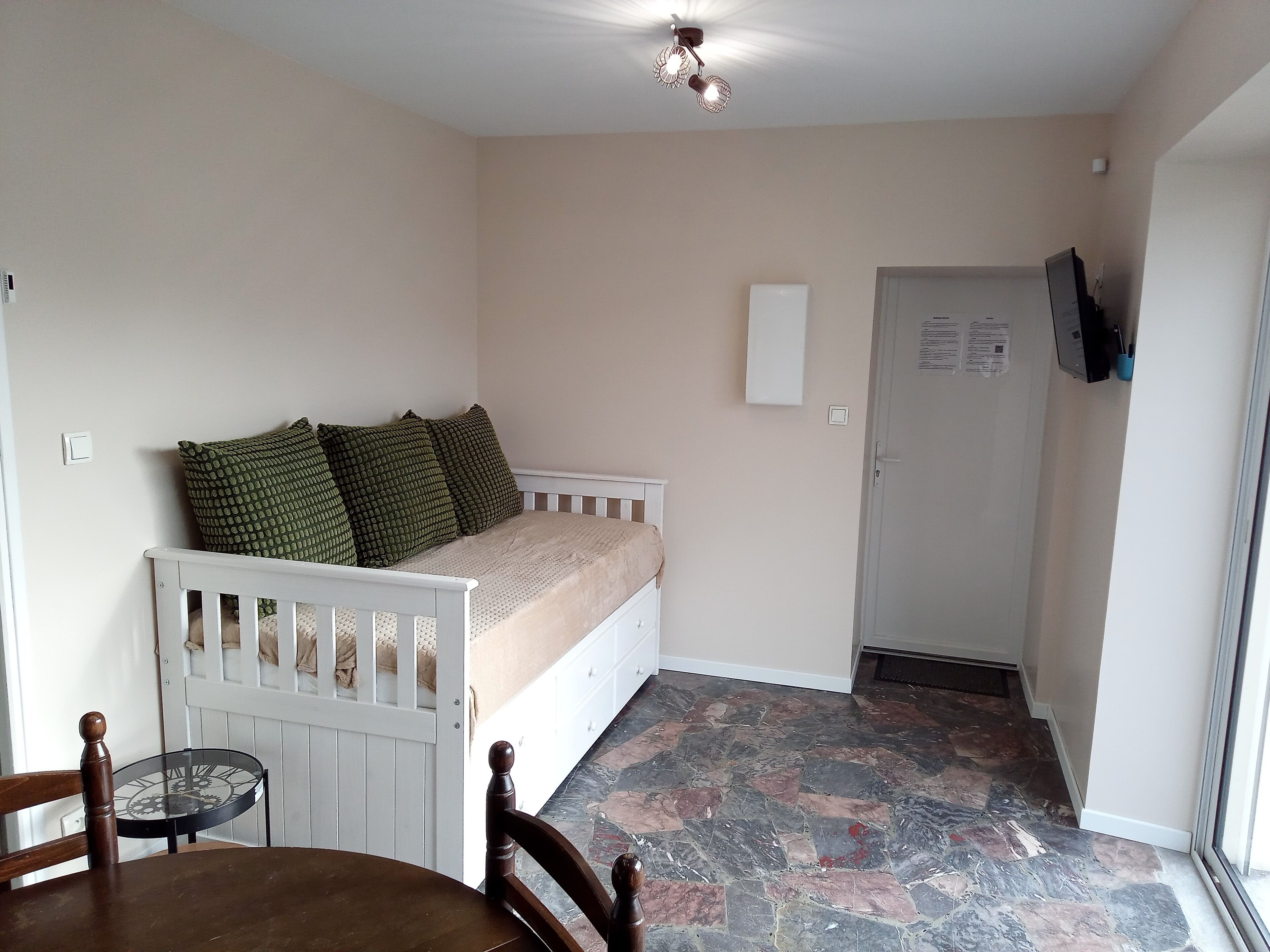 Una habitación pequeña y acogedora con una cama, una silla, una mesita y una puerta.