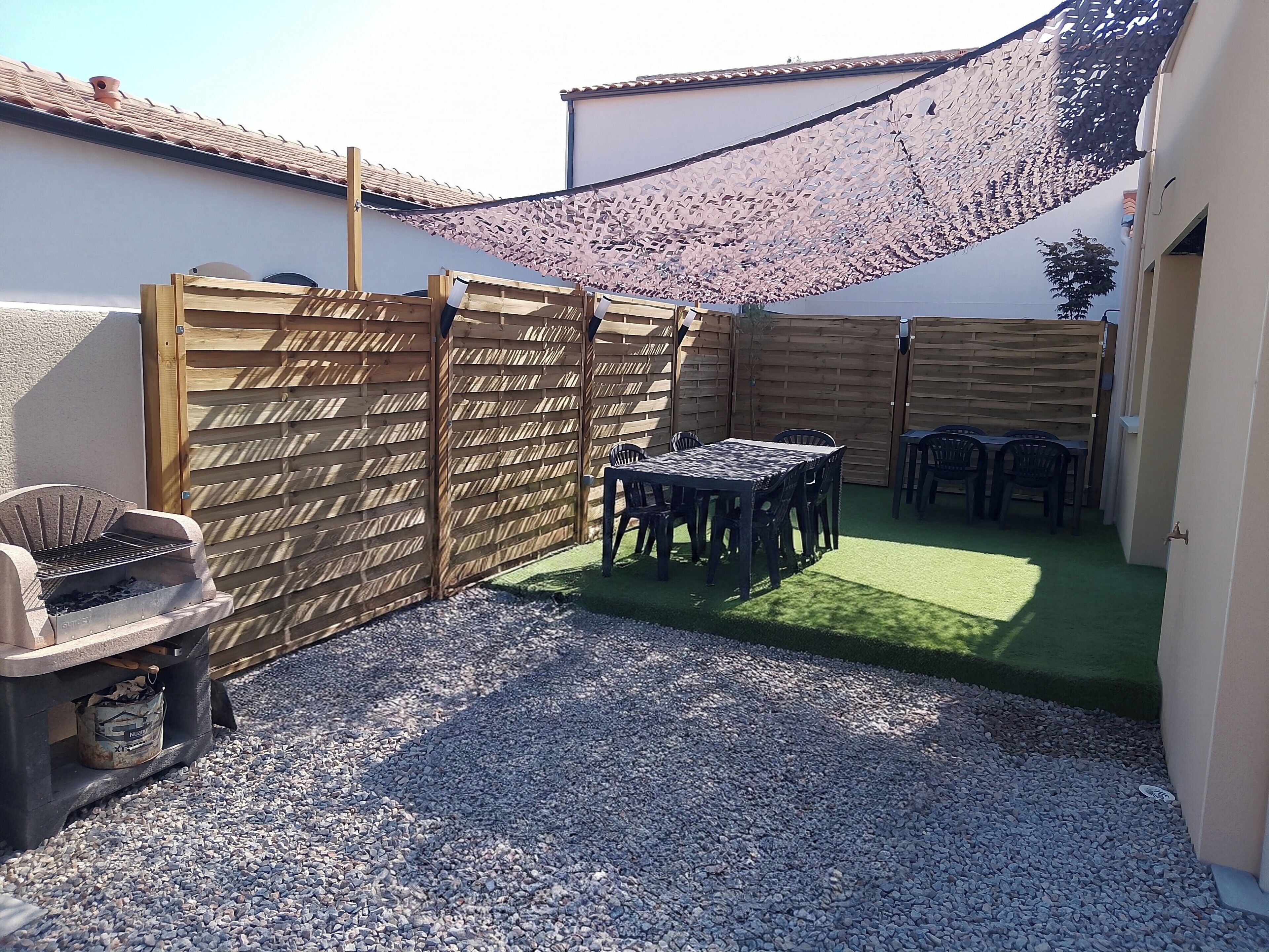 Un patio con mesa y sillas, una parrilla y una valla de madera.