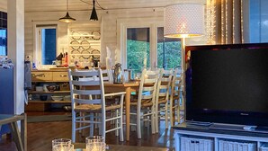Un comedor acogedor con una mesa de madera, sillas blancas y un televisor en un mueble.