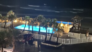 Una vista notturna di un resort con piscina, palme e un gazebo.