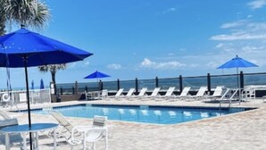 Un'area piscina con lettini e ombrelloni, un pavimento piastrellato e vista sull'oceano.