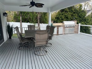 Eine überdachte Terrasse mit Esstisch und Stühlen, einem Deckenventilator und einem Grill.