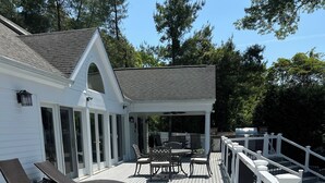 Un pontile in legno con una veranda coperta, arredi da esterno e un edificio bianco con un garage.