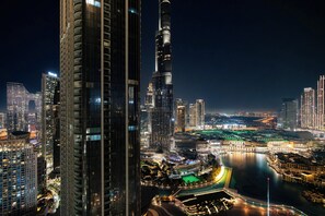 A nighttime cityscape with high-rise buildings, including a prominent tower with illuminated windows and a waterfront area with a green-lit structure.