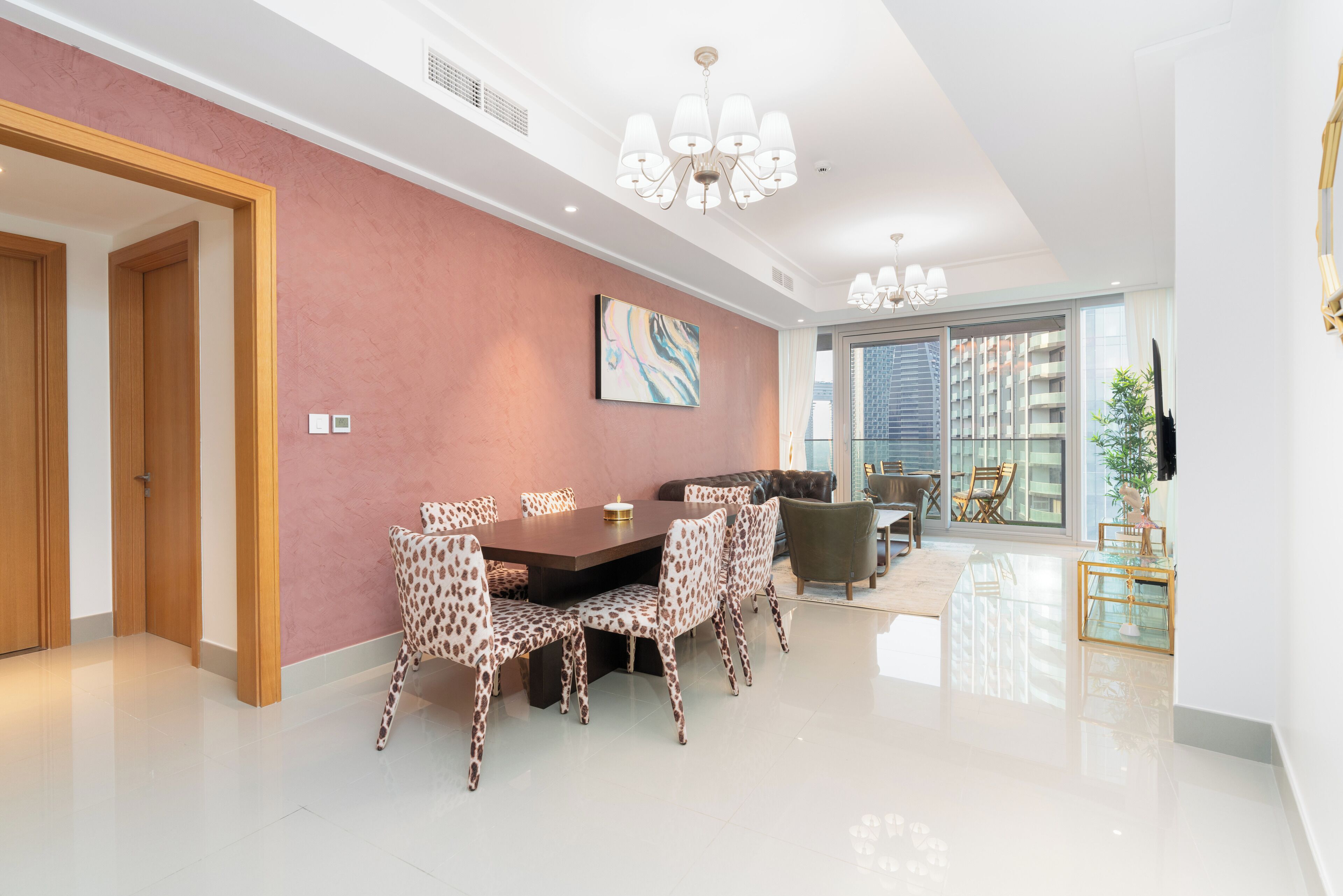 A modern dining area with a large table and leopard print chairs, a chandelier, and a city view through large windows.