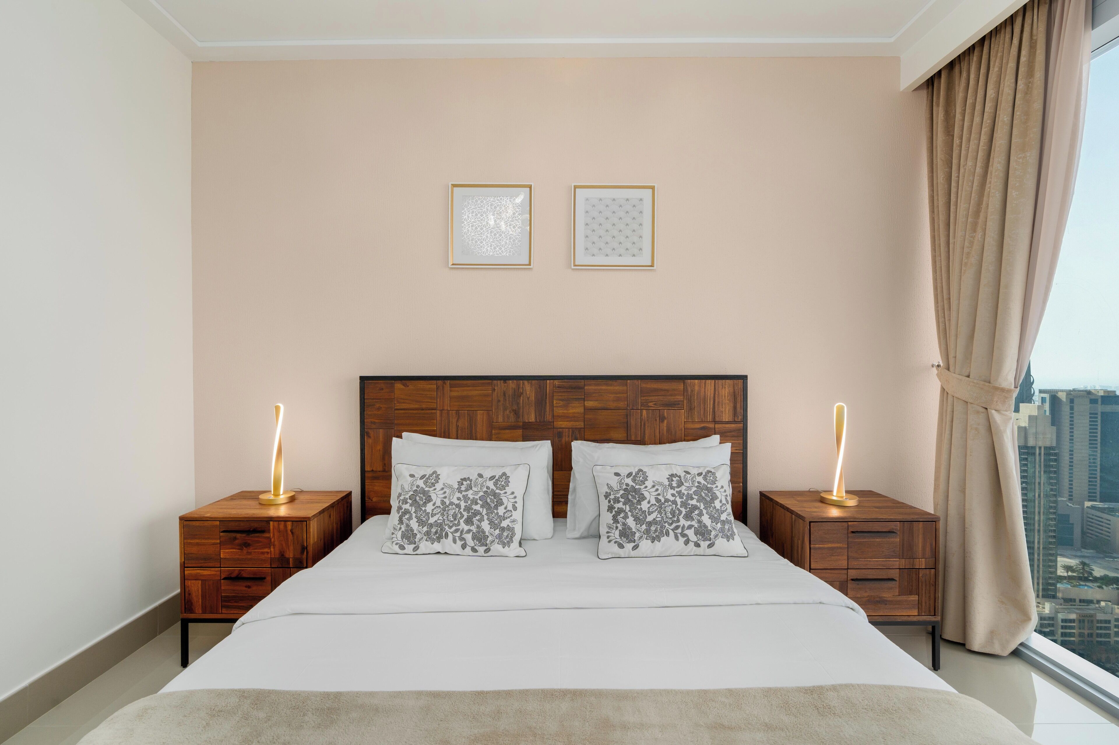 A bedroom with a wooden headboard, two bedside tables with lamps, a bed with white bedding, and two framed pictures on the wall.