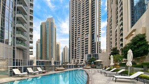 A rooftop swimming pool with lounge chairs and umbrellas, surrounded by high-rise buildings. - Lux BnB Opera Grand Burj Khalifa & Fountain View (Dubai)