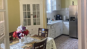 Une cuisine avec des meubles blancs, un réfrigérateur en acier inoxydable et un coin repas comprenant une table et des chaises.