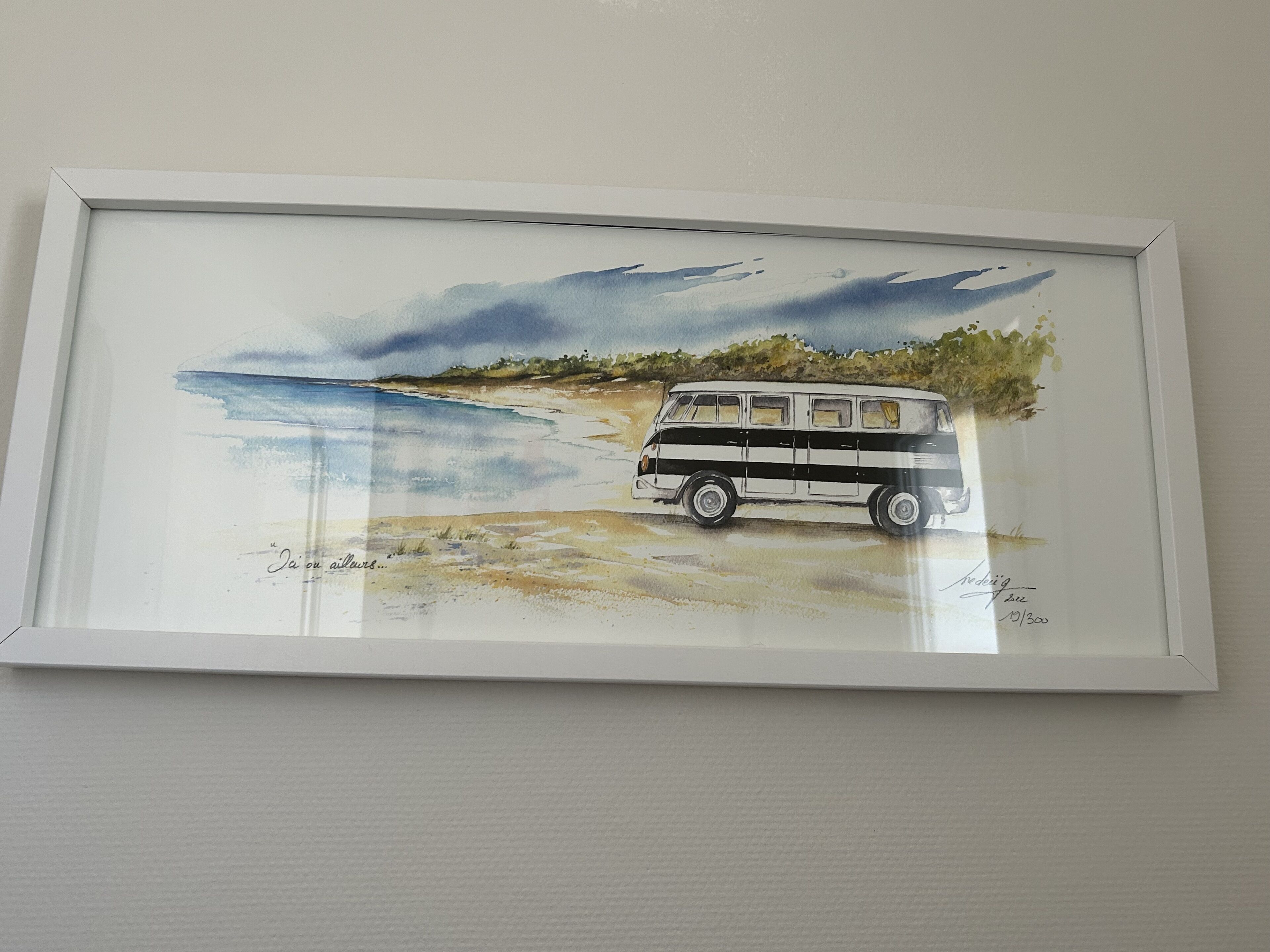 A framed watercolor painting of a van parked on a beach with a cloudy sky.
