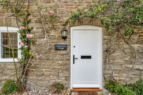 A stone building with a white door, a sign reading "Lower Farm Cottage," and a window to the left.