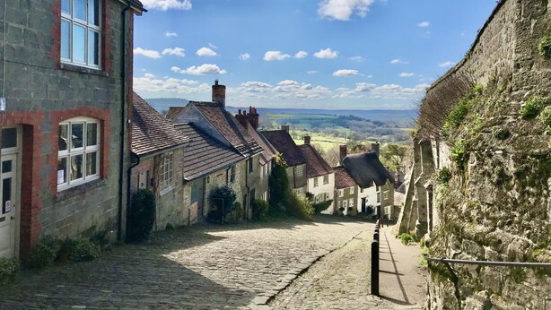 A narrow cobblestone street flanked by historic stone buildings with traditional pitched roofs and chimneys. - Lower Farm Cottage -  Stalbridge Weston, Sherborne (Sturminster Newton, Dorset)