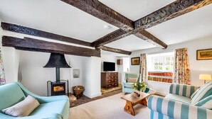 A cozy living room with exposed wooden beams, a fireplace, a sofa, a coffee table, and a television. - Lower Farm Cottage -  Stalbridge Weston, Sherborne (Sturminster Newton, Dorset)