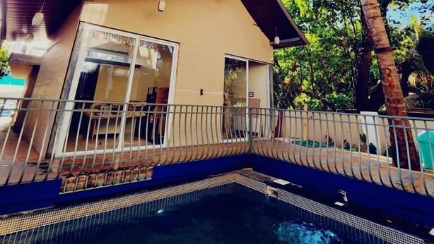 A pool area with a house in the background, surrounded by palm trees. - Adrista Divine Cottages (Arambol)