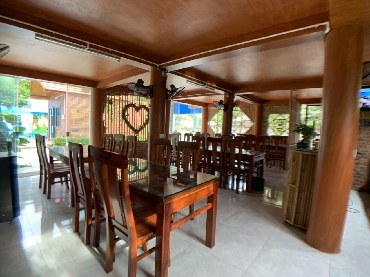 A spacious dining area with wooden tables and chairs, a heart-shaped decoration on the wall, and a view of the outdoors.
