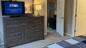 Een slaapkamer met een donker houten dressoir, een televisie waarop 'technicolor' staat, een lamp en een deur naar een andere kamer.