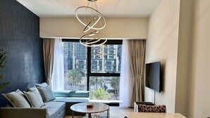A modern living room with a sofa, a coffee table, a dining table with leopard print chairs, a TV mounted on the wall, and a large window with curtains. - LuxBnB Dubai Opera Act-1 Boulevard Views (Dubai)