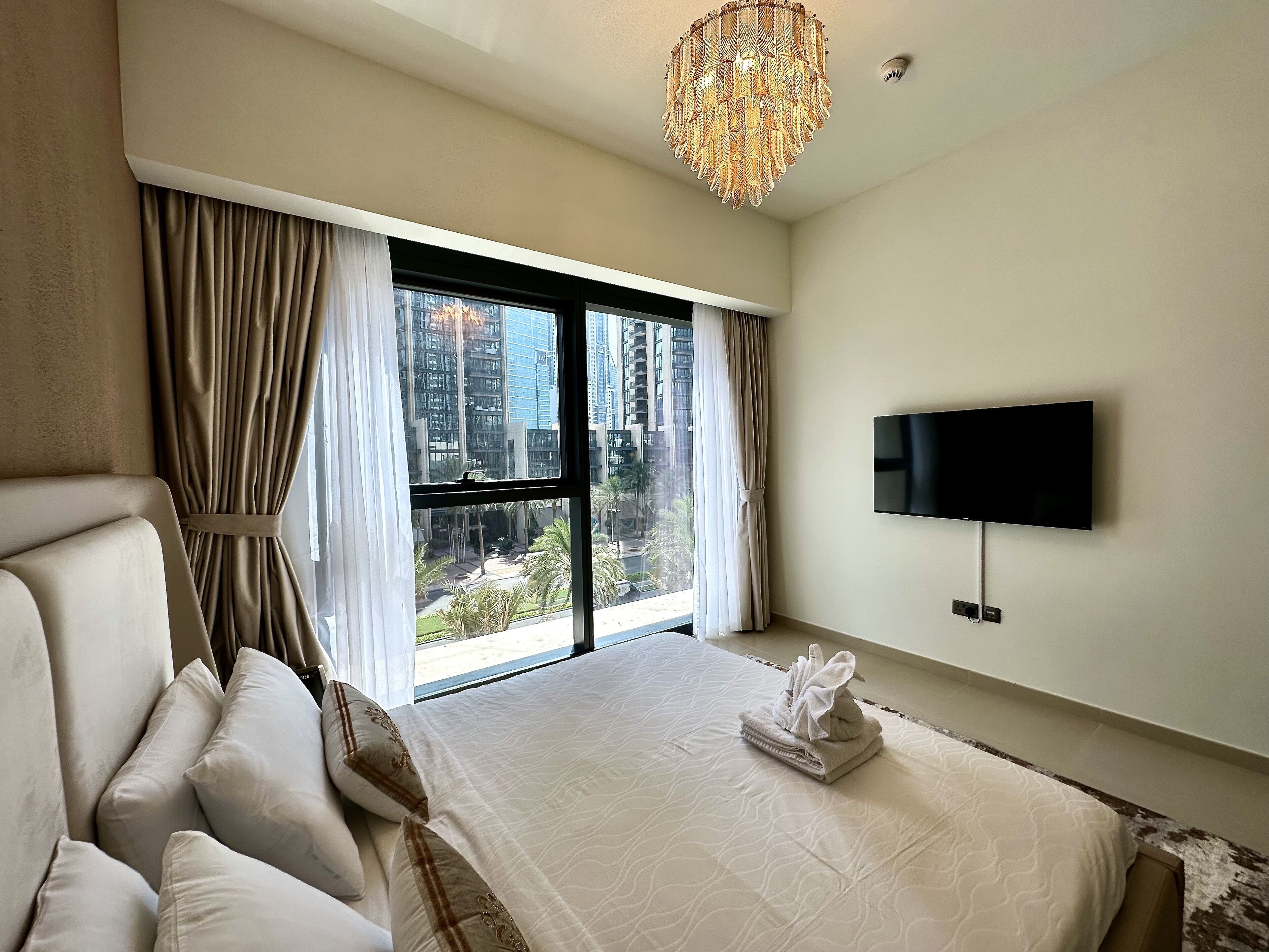 A hotel room with a large bed, a TV mounted on the wall, and a view of tall buildings outside the window.