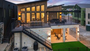 Een modern gebouw met twee verdiepingen, een balkon, terras en uitzicht op een waterlichaam.