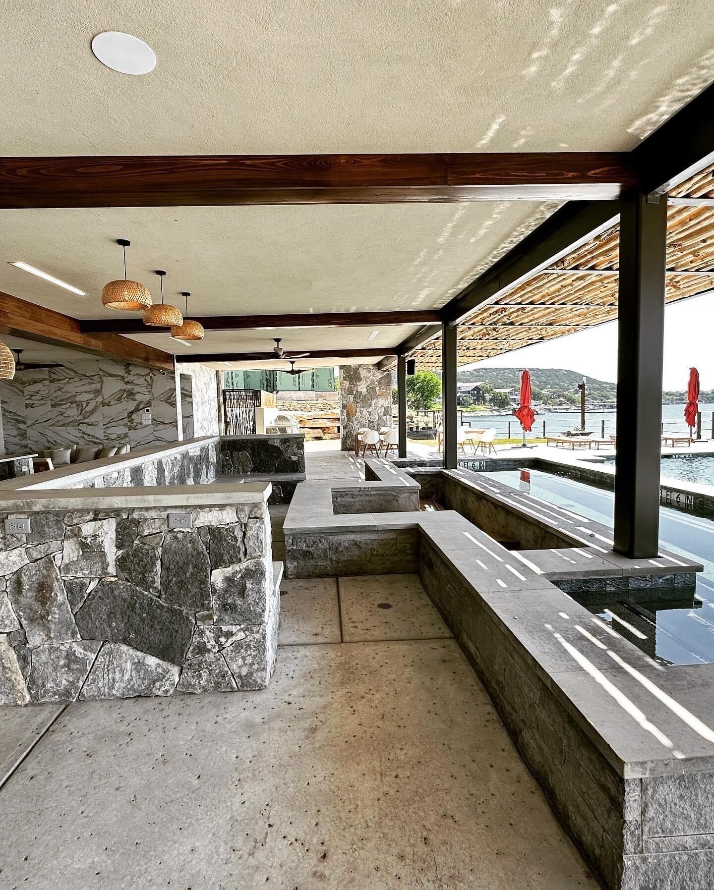 A modern outdoor bar area with stone countertops, seating, and a view of the water.