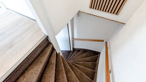 Een spiraaltrap met beklede treden, houten leuningen en een witte muur met een houten paneel erboven.