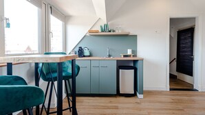Een kleine keuken met smaragdgroene stoelen, een houten tafel en een klein aanrecht met keukengerei.