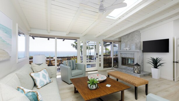 A spacious living area with a wooden coffee table, a sofa with patterned cushions, a bench, and a flat-screen TV mounted on the wall. - Historic Olde Del Mar Hacienda | Panoramic Ocean Views (Del Mar)