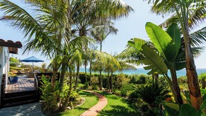 A tropical garden with a paved path leading to a wooden deck with outdoor furniture. - Historic Olde Del Mar Hacienda | Panoramic Ocean Views (Del Mar)