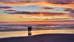 Eine Strandansicht mit zwei Personen, die am Ufer stehen und den Sonnenuntergang über dem Meer betrachten.