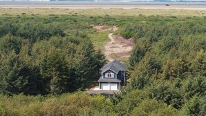 Ein Haus mit Garage, umgeben von dichtem Wald, das zu einem Strand mit freiem Blick auf den Ozean führt.