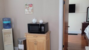 Una habitación pequeña con un microondas sobre un mueble de madera, un dispensador de agua y un cubo de basura.