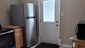Una cocina compacta con un refrigerador de acero inoxidable, un microondas y un pequeño armario de madera.