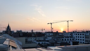 A cityscape at sunset with a prominent cathedral and construction cranes.