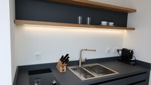 A modern kitchen with a stainless steel sink, a knife block, a coffee machine, and a shelf with cups and glasses.