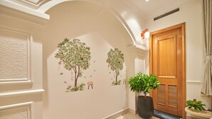 A hallway with a wooden door, a potted plant, and wall decals of trees and animals. - Bin Bin 10 - Mimosa Hotel near Tan Son Nhat Airport (Ho Chi Minh City)