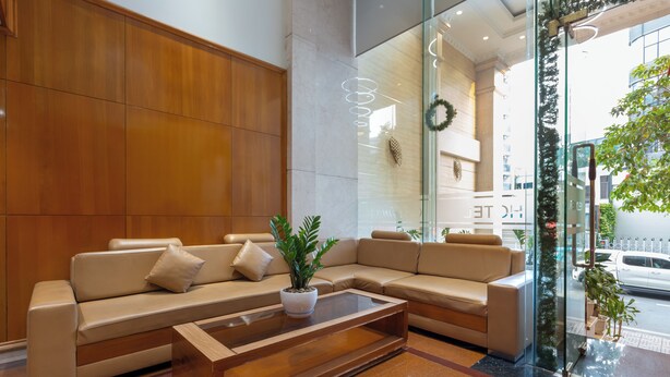 A modern lobby with a beige sectional sofa, a glass wall with a view of the street, and a wooden wall. - Bin Bin 10 - Mimosa Hotel near Tan Son Nhat Airport (Ho Chi Minh City)