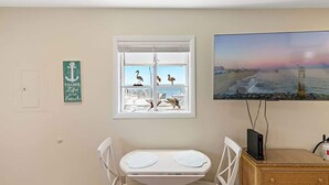 A room with a window overlooking a beach, a painting of a sunset, and a small table with chairs. - Ocean & Bay Views, Steps to Beach (Ocean City)