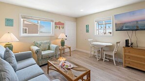 A living room with a sofa, a coffee table, a dining table with chairs, and artwork on the walls. - Ocean & Bay Views, Steps to Beach (Ocean City)