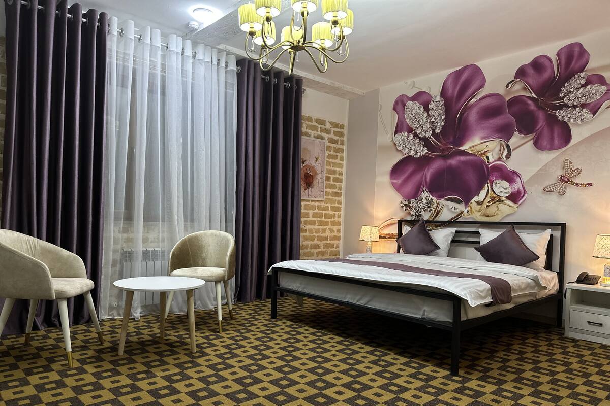 Ein Schlafzimmer mit einem gemusterten Boden, einem Bett mit Kopfteil, zwei Stühlen, einem Tisch und einer Pendelleuchte.