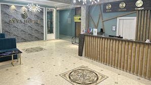 A hotel reception area with a marble wall, a reception desk, a chandelier, and a blue sofa. - Ayva Hotel (Tashkent)