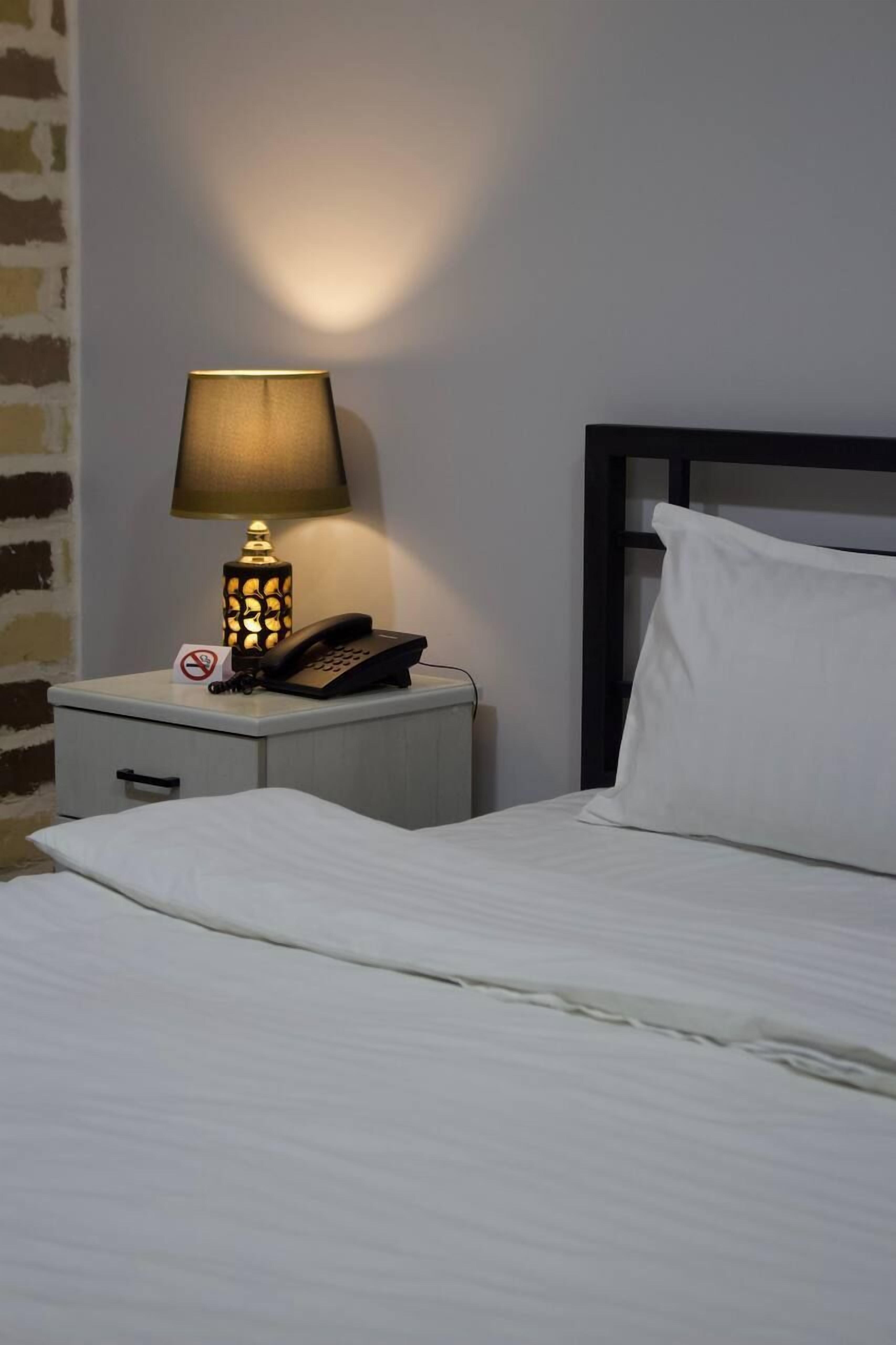 Un lit bien fait, avec un oreiller blanc, une table de chevet sur laquelle se trouve une lampe et un téléphone.