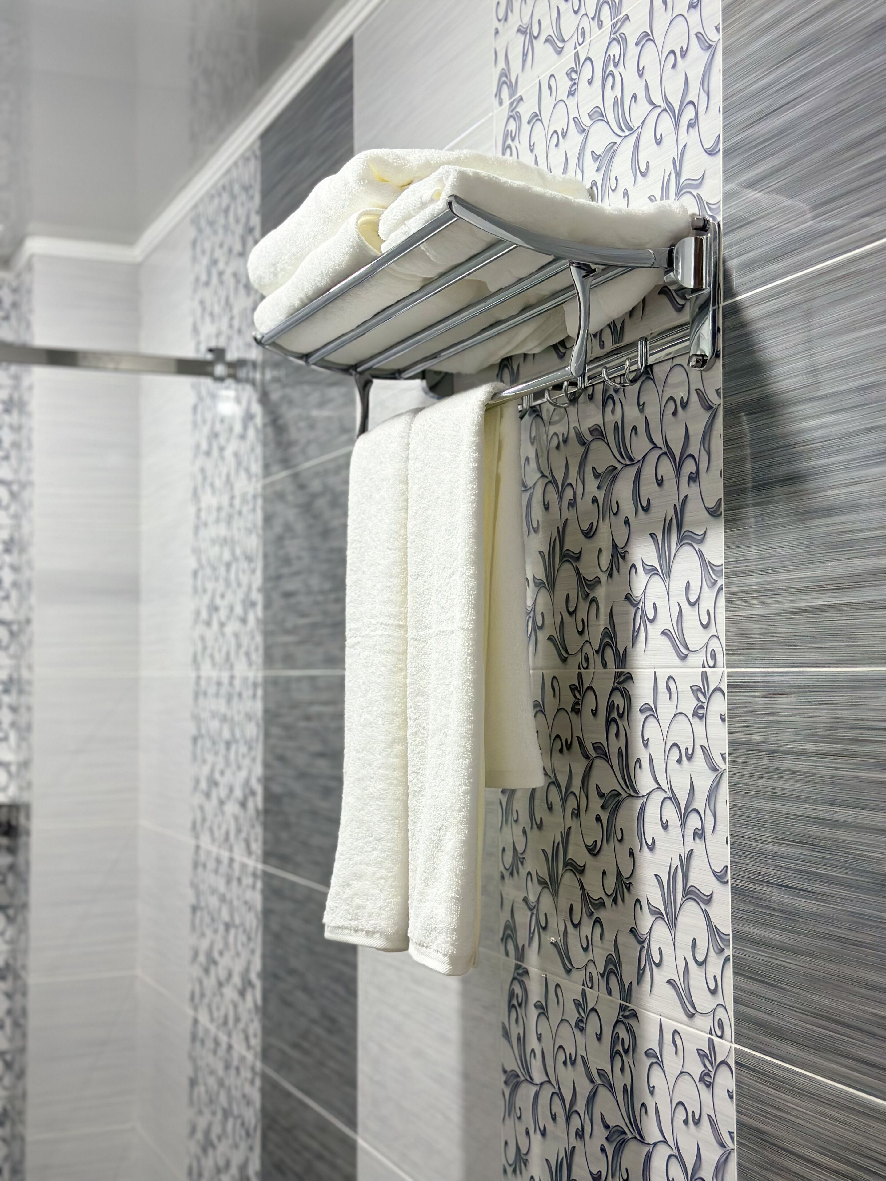 Une salle de bain avec un porte-serviettes sur lequel sont posées deux serviettes blanches et un rideau de douche orné d’un motif floral noir.