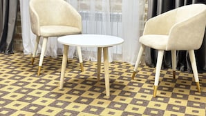 Two beige chairs and a small round table in a room with a patterned floor and sheer curtains. - Ayva Hotel (Tashkent)