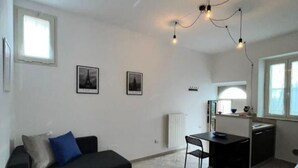 A compact living space with a black sofa, a small dining table, and a kitchenette area.
